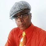 Campbell X headshot. Campbell is a Black butch person, shown from the shoulders up. They are wearing a grey tweed flat cap, horn rimmed spectacles and a bold bright orange shirt with a golden yellow tie. They are looking at the camera.